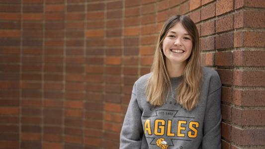A women wearing a CSI sweatshirt leans against a brick wall.